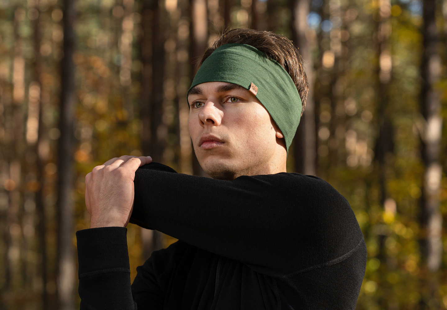 Man wearing a green merino wool Menique headband outdoors with trees in the background