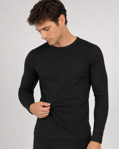 A medium studio shot of a man wearing a black long-sleeved thermal shirt and black leggings, looking down while gently pulling on the front hem of the shirt.