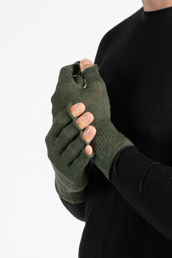 A person wearing a black long-sleeved shirt is shown from the chest up, putting on dark green fingerless gloves. The background is white.