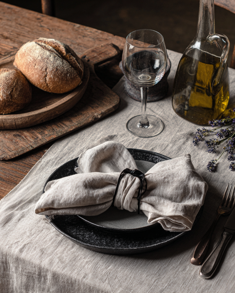 Natural linen table runner with rustic dinnerware, bread and lavender on wooden dining table.