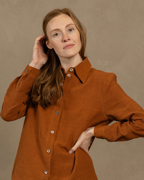 Woman with long hair wearing an almond brown linen menique button-up shirt against a beige background