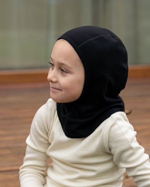 Child wearing black merino wool balaclava and cream long-sleeve base layer indoors