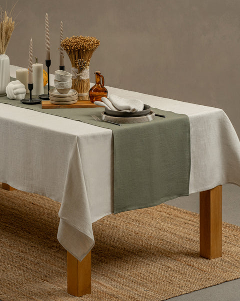 The stone green linen table runner on top of a wooden table, captured in a close up picture from the corner of the table. 