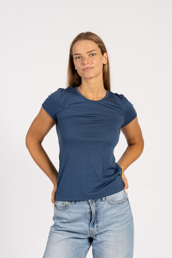 A woman standing facing forward in a blue t-shirt and jeans, with both hands on her hips.