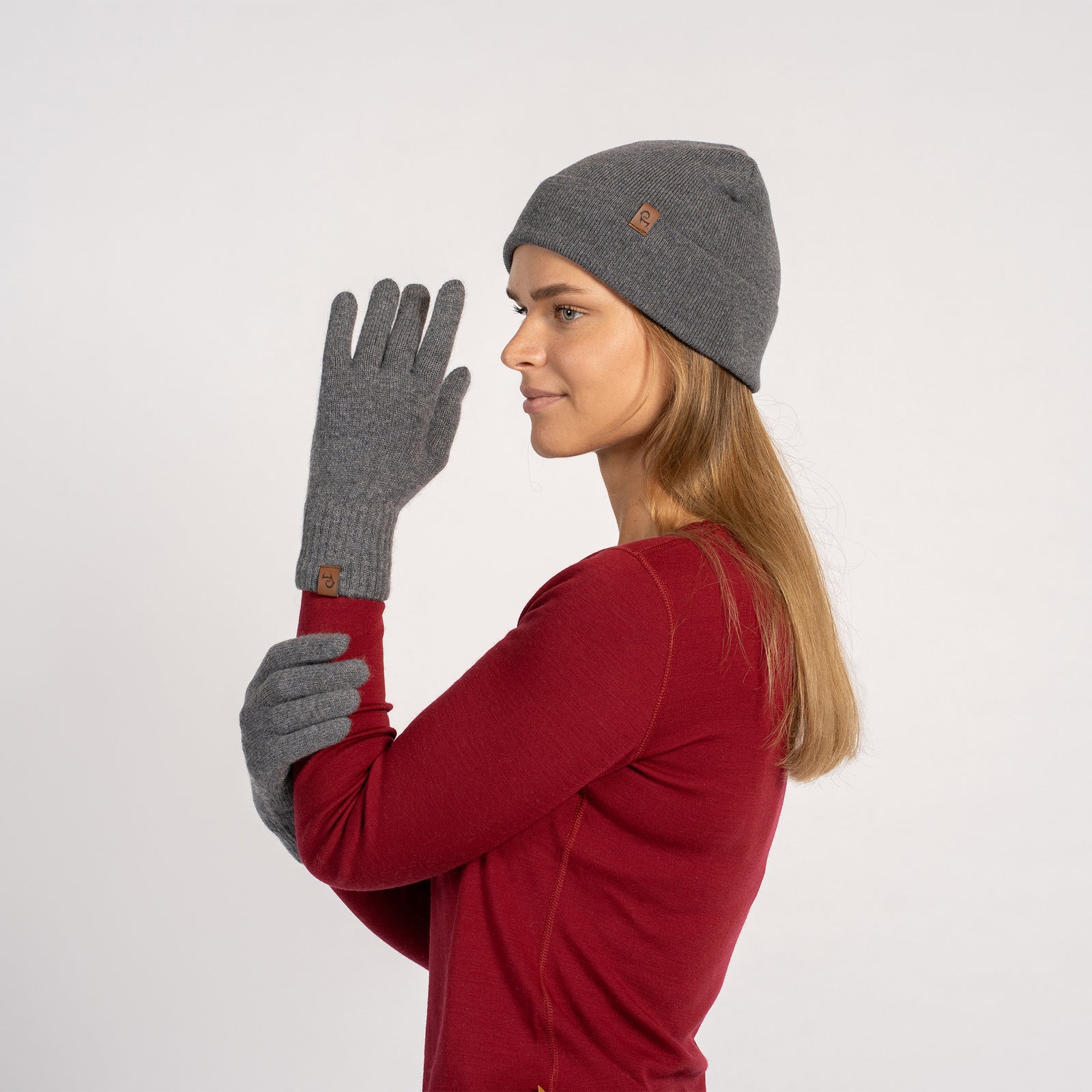 Woman wearing a creamy beige cashmere beanie and matching short gloves, side profile view, adjusting the glove.