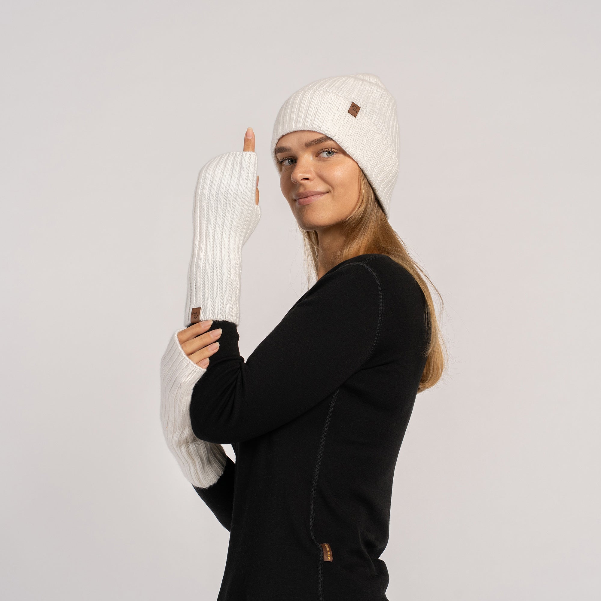 Full-length shot of woman in black top and jeans wearing white beanie and long white wrist warmers, facing camera.