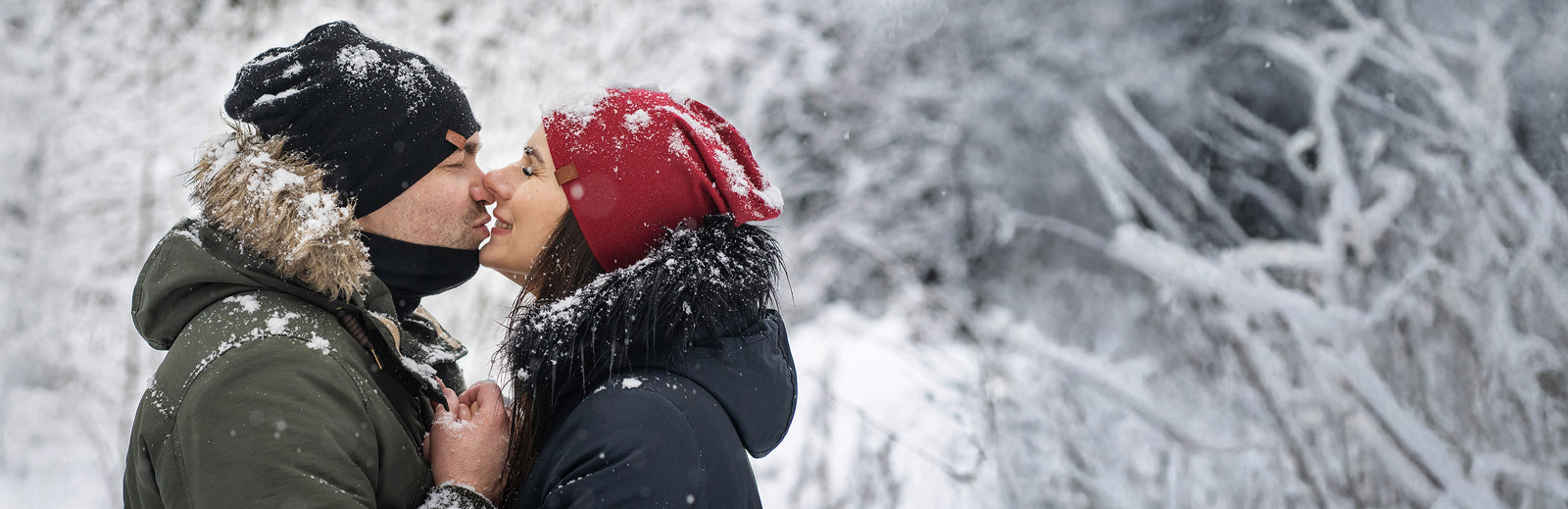 Couple wearing Merino wool beanies sharing a moment outdoors in snowy winter landscape