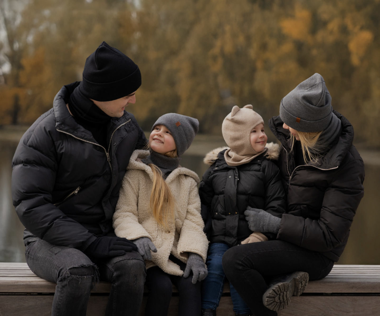 Family of four sitting together outdoors in winter clothing with a blurred natural background.