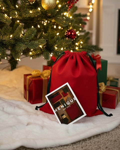 Red gift bag with a card under a decorated Christmas tree.