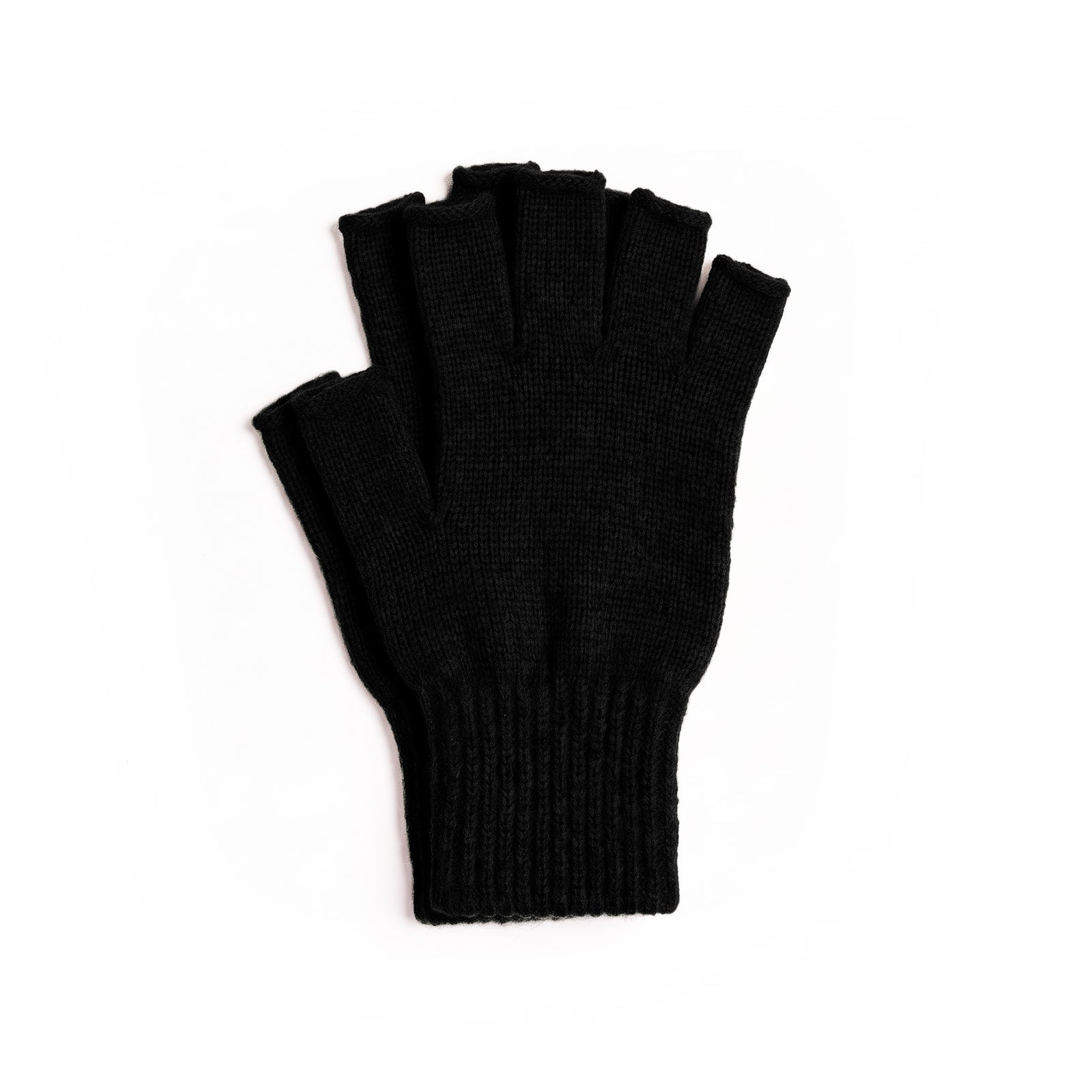 A close-up of a person's hands wearing black knit fingerless gloves, crossed in front of a beige winter coat and a white ribbed sweater outdoors.