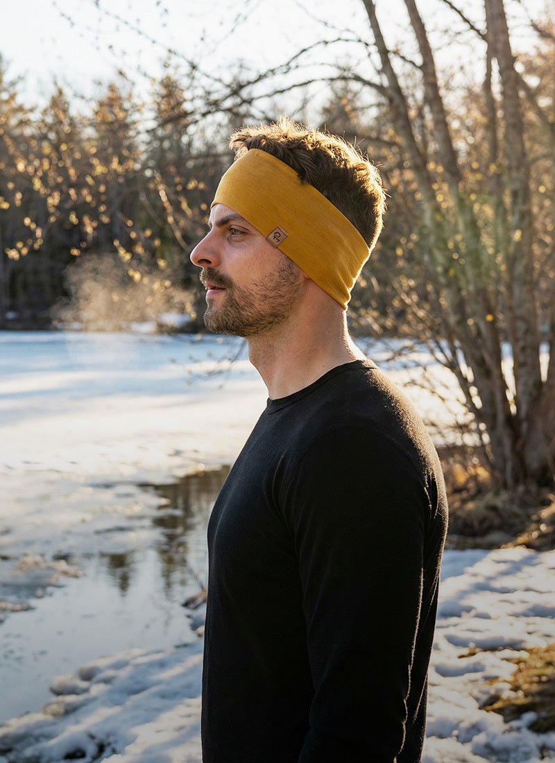 Man wearing a yellow headband standing by a snowy landscape with trees.