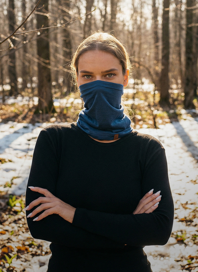 Person wearing a blue face mask and black sweater in a snowy forest