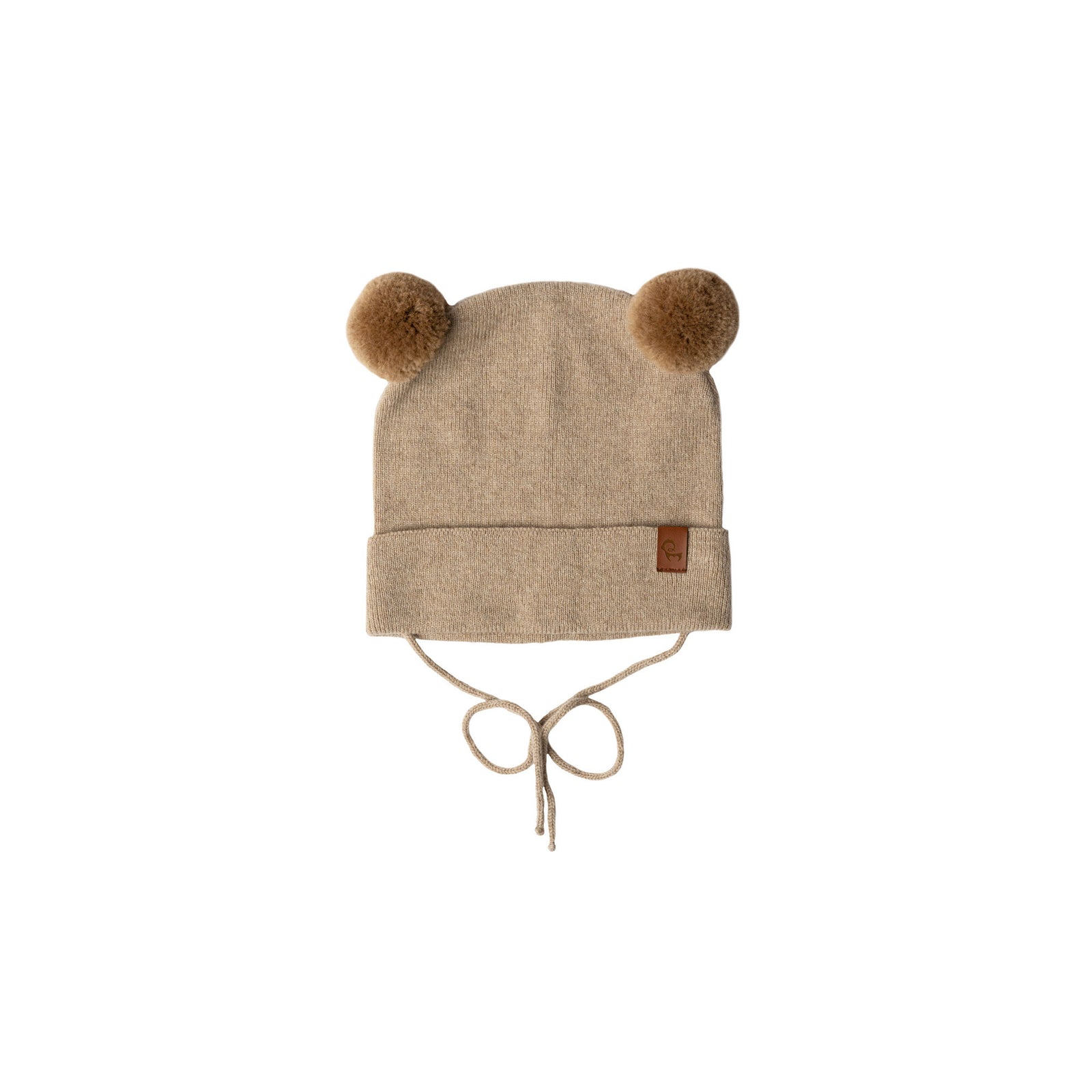 A young child with blue eyes and a slight smile, looks directly at the viewer. They are wearing a beige knit hat with brown pom-pom ears, a beige turtleneck or neck warmer, and a light pink sherpa-style coat. The background is a blurred outdoor scene with muted green and brown tones.