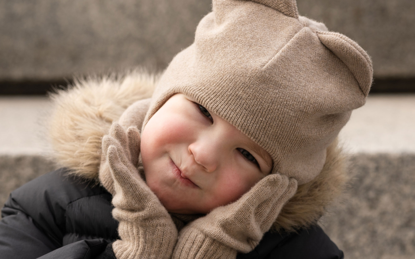 A toddler girl wearing the menique merino wool knit gloves and balaclava with ears in creamy beige color.