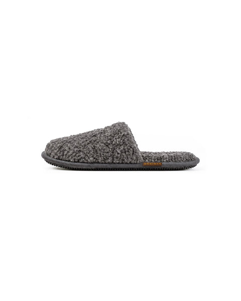 A side view of a single dark gray fuzzy slip-on slipper with a dark gray insole, a flat black sole, and a brown "MENIQUE" tag on the side.
