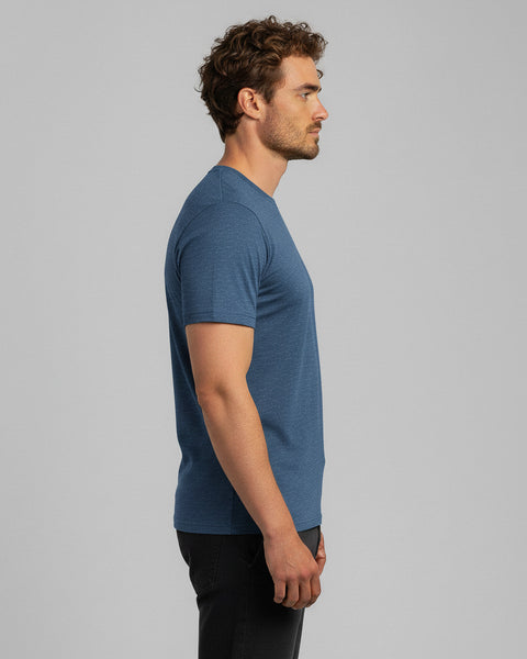 A side profile of a man wearing a blue T-shirt and black jeans, standing against a neutral gray background.