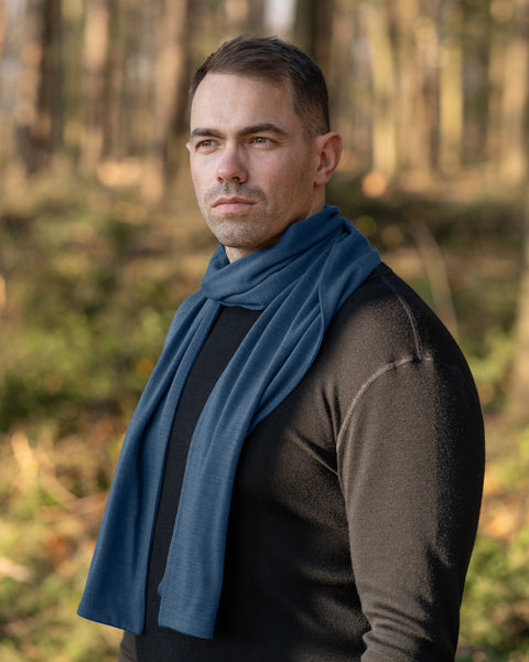 Man wearing a blue merino wool scarf on black merino long sleeve shirt standing in a forest
