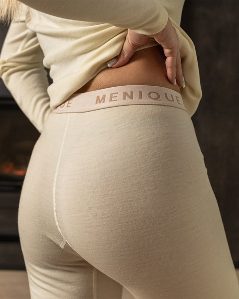 Merino wool pants are a natural color and are made of a smooth, soft fabric. They have a straight leg fit and rubber band. The waistband is a contrasting lighter color. There are no visible pockets or embellishments