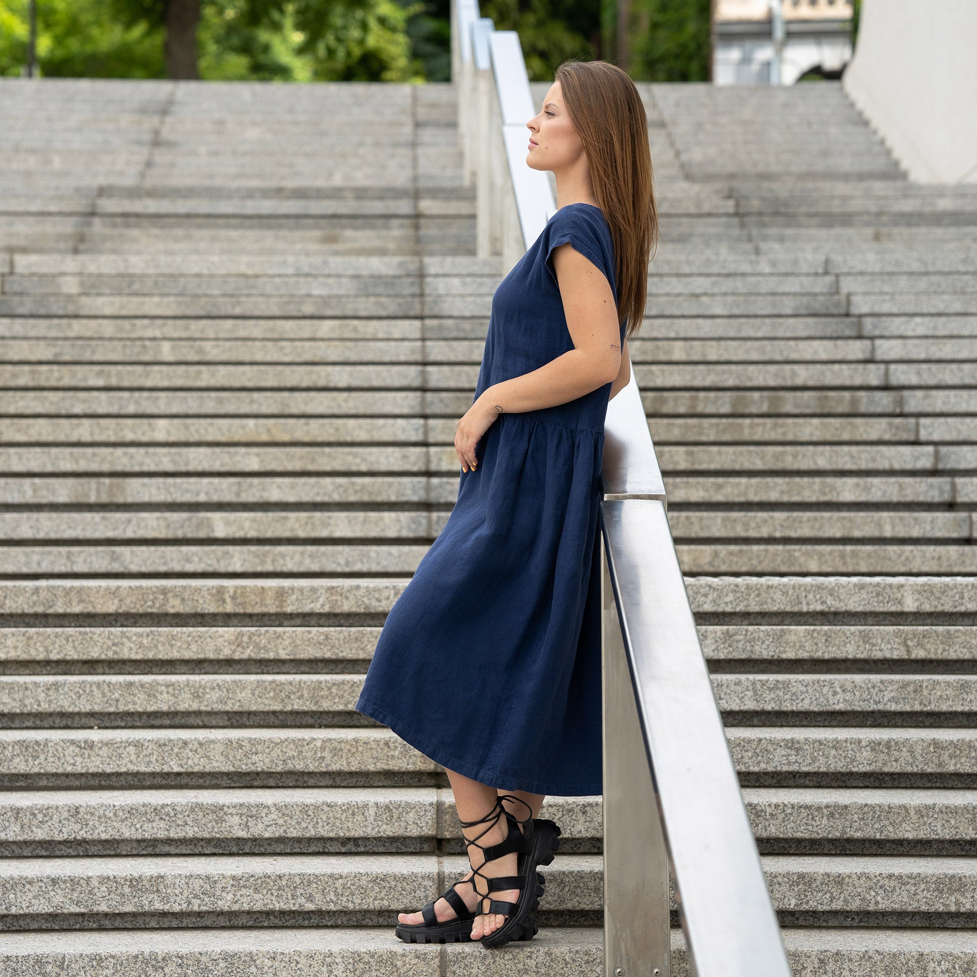 Young woman posing in a city street on stears wearing linen smock dress cecilia in a storm blue color.