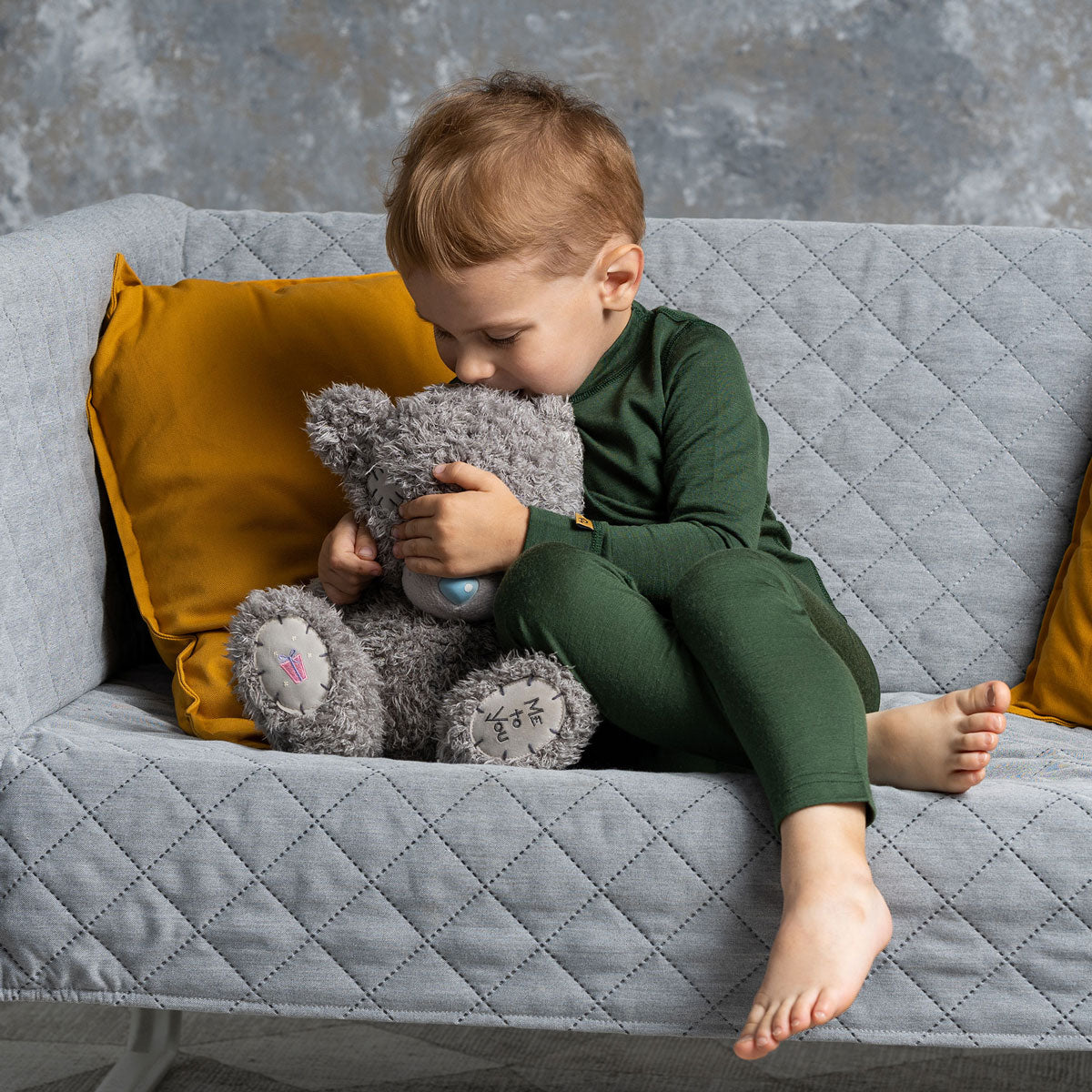 A smiling baby wearing natural merino thermal pants and a matching long-sleeve top, standing against a white background.