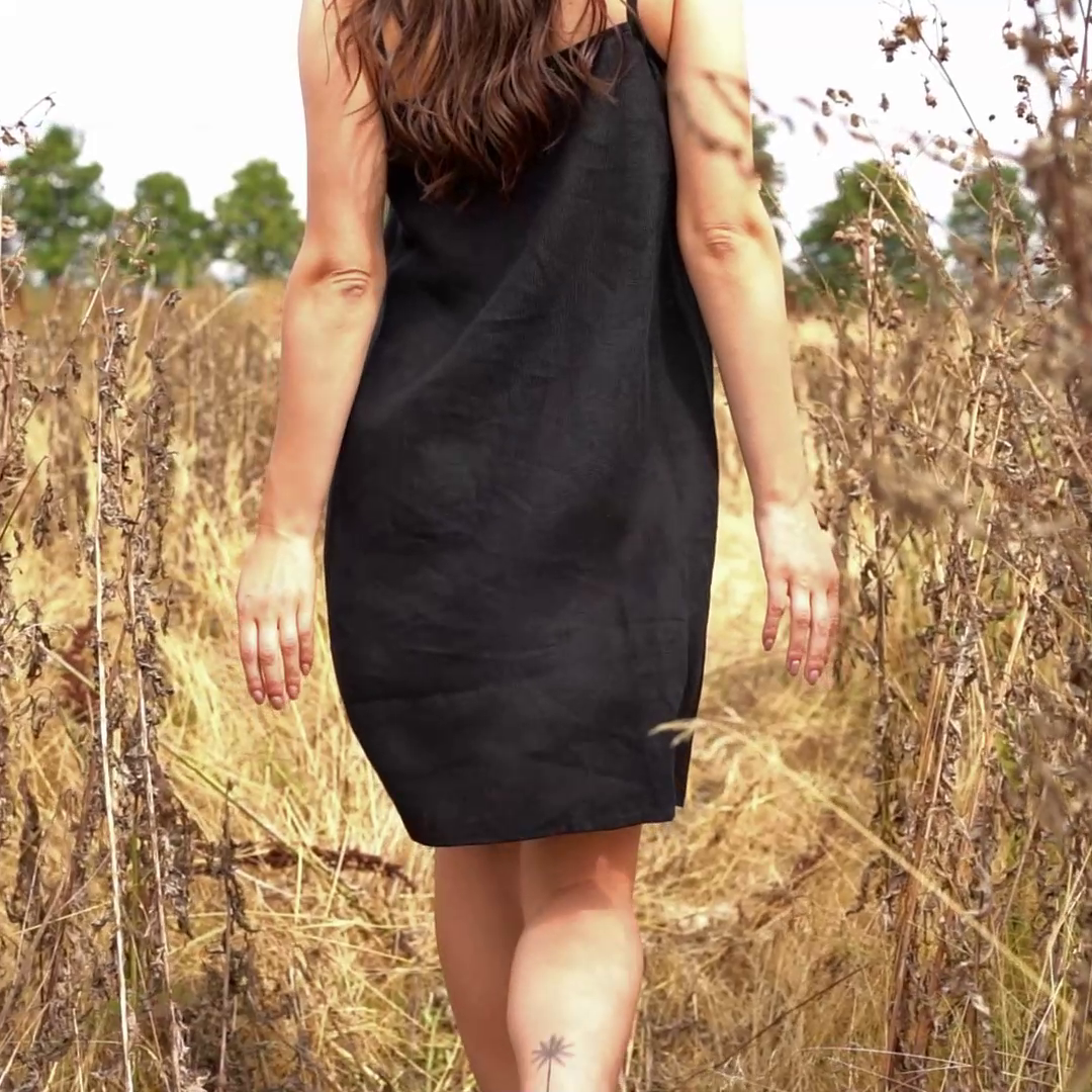 Woman walking through tall grass while wearing linen slip dress in b;ack color